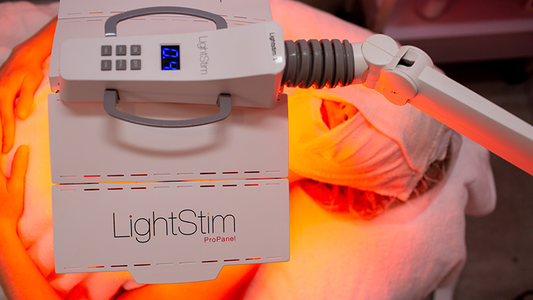 Woman receiving LightStim anti-aging LED therapy in a tranquil Santa Barbara med spa, with soft red and amber light illuminating her face during treatment.